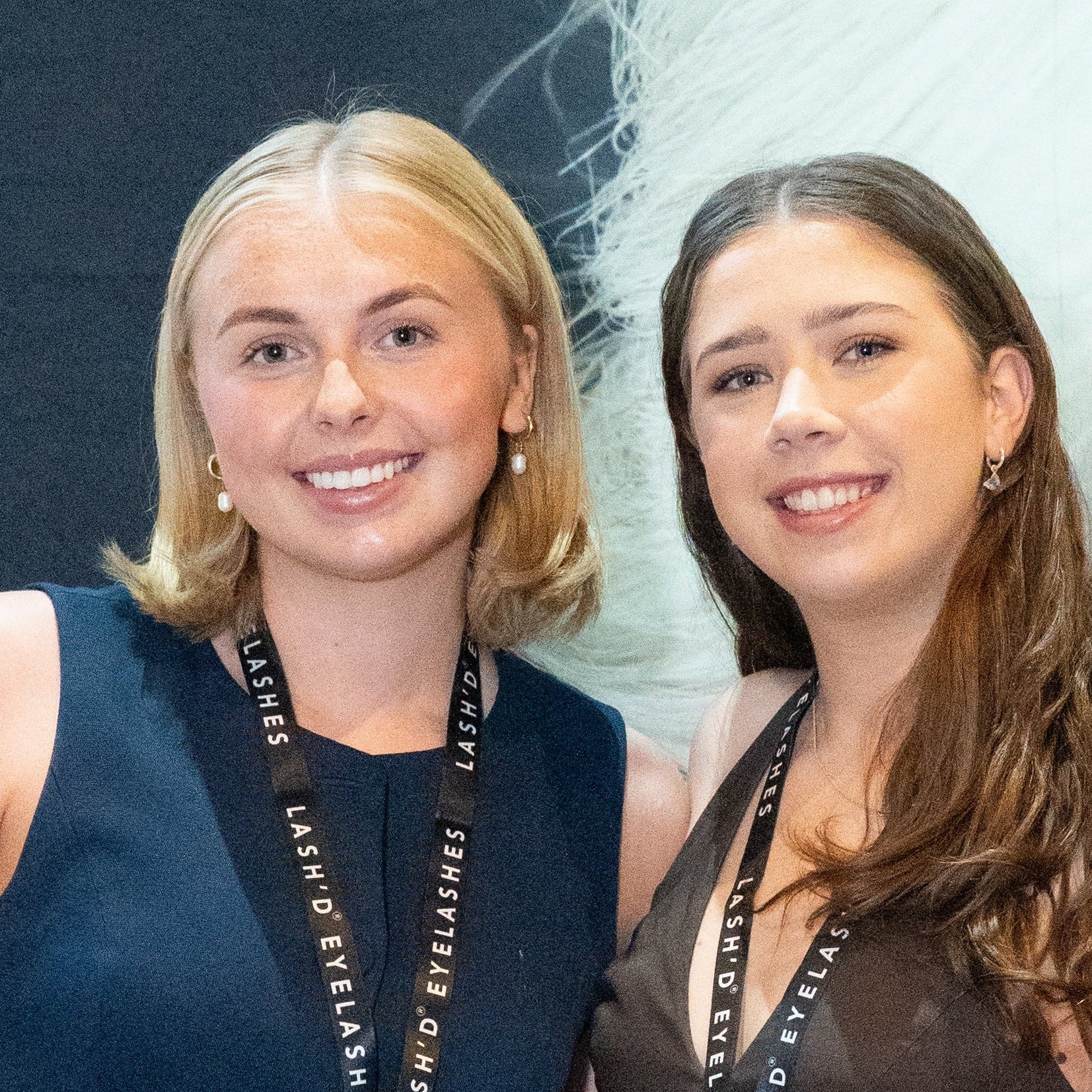 Two women standing behind a display of products with 'runway Lash Co.' branding in the background.