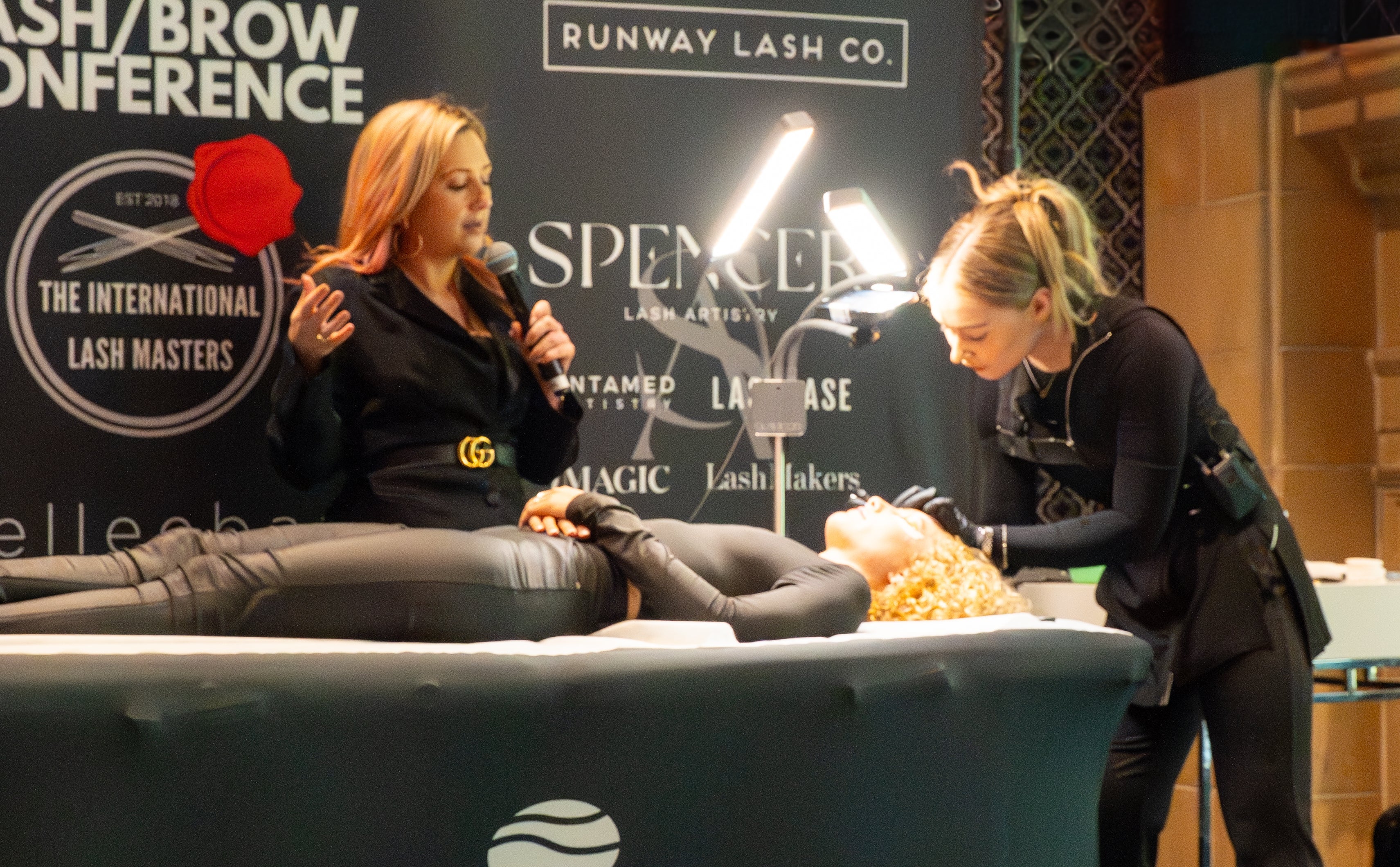 Woman receiving lash treatment at a lash and brow conference with 'elleebana' branding.
