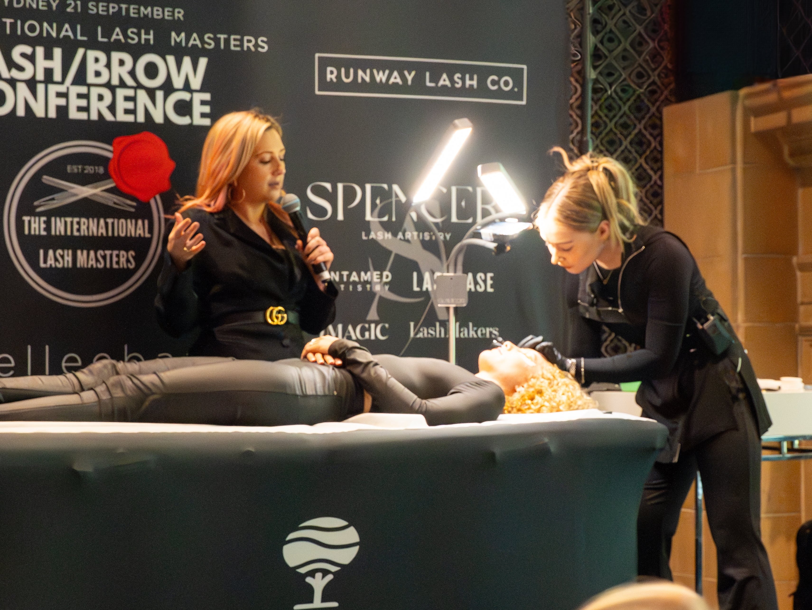 Woman receiving lash treatment at a lash and brow conference with 'elleebana' branding.